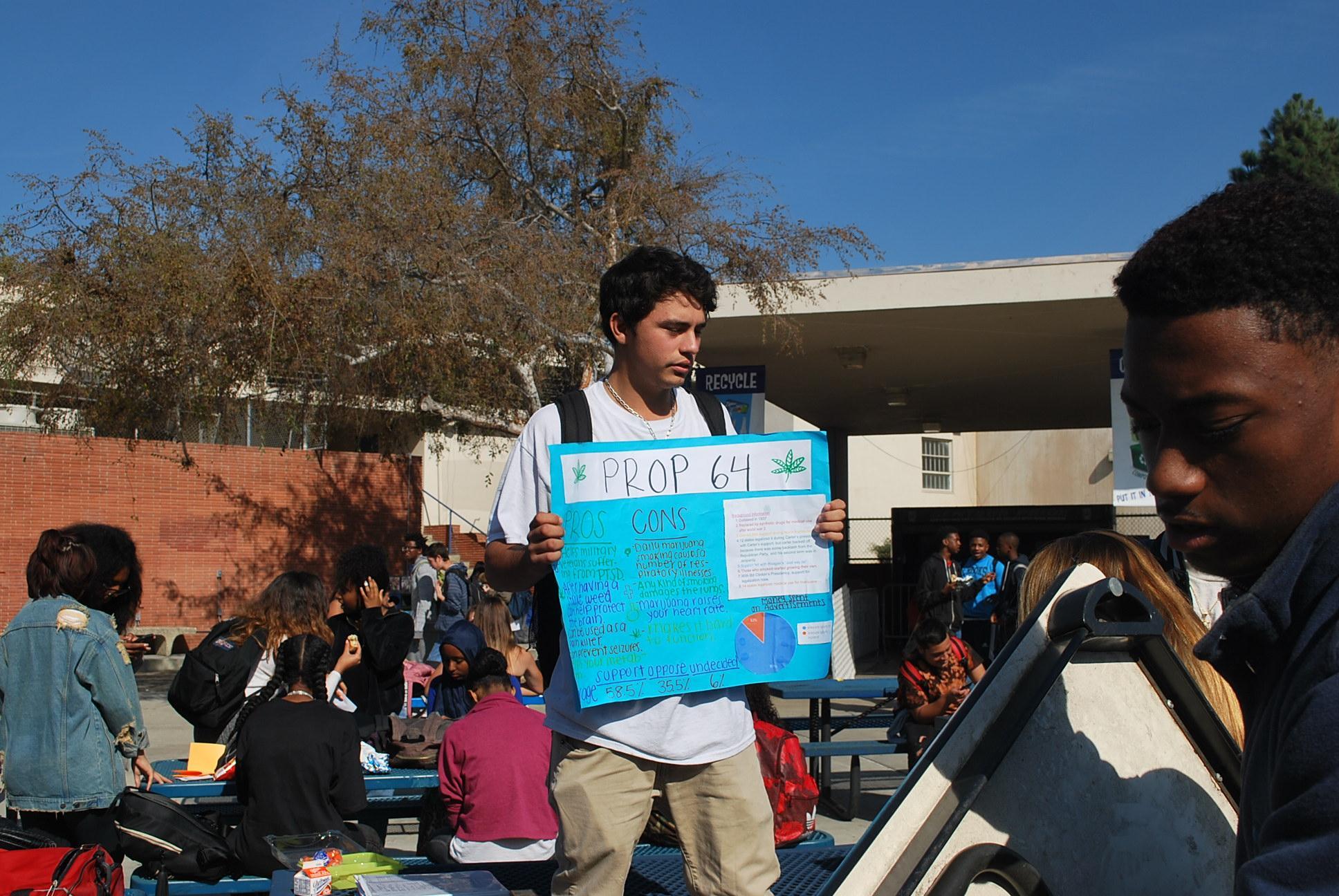 Students shows poster with pros and cons of Proposition 64 around the lunch patio
