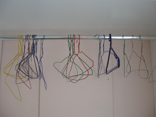 an empty wardrobe with various coloured metal coat hangers hanging on a rail